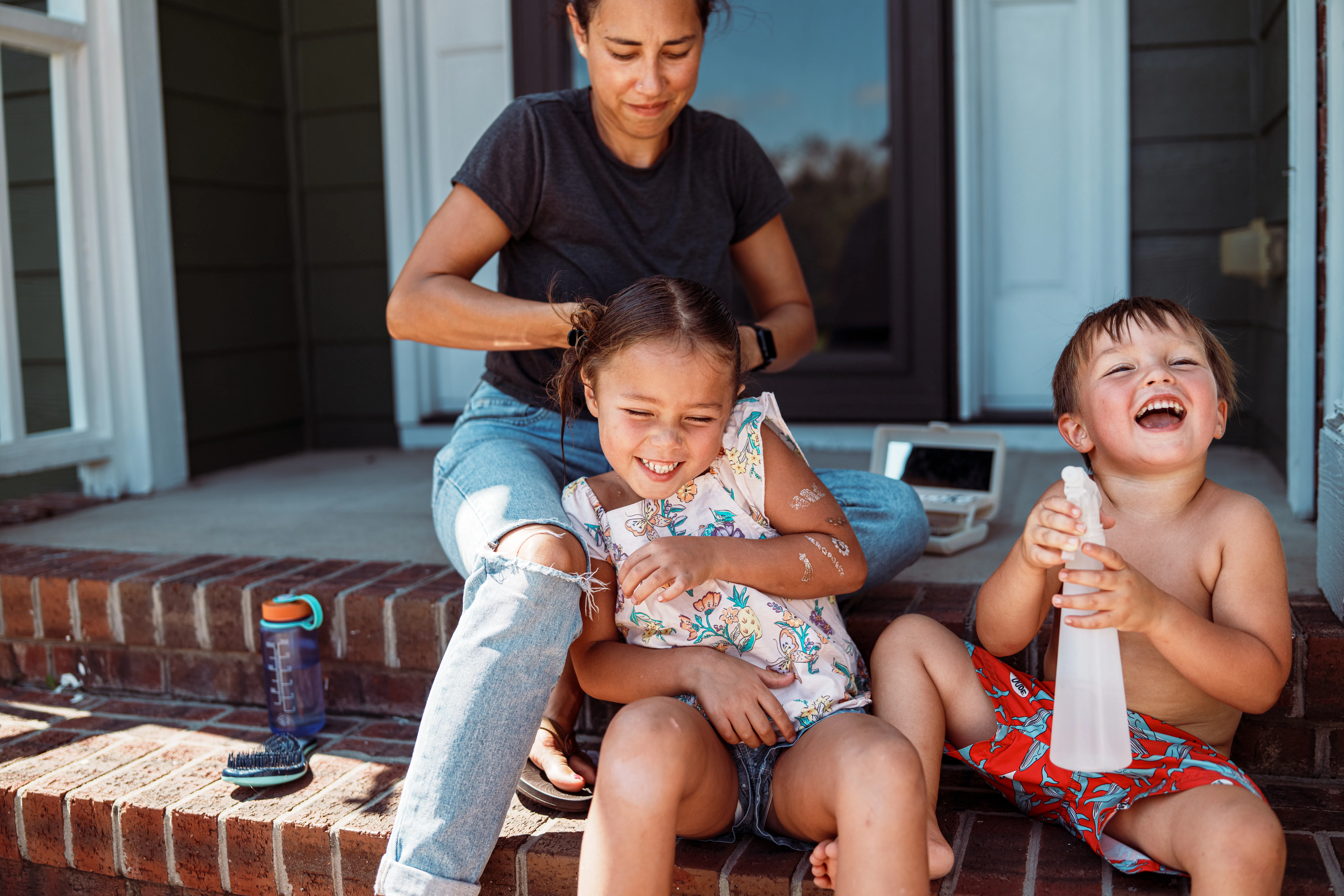 A five-year-old Eurasian girl sits on the front steps of her suburban home with her playful little b...