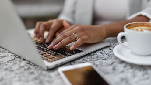 Close-up of Black woman's hands using a laptop while working remotely from a coffee shop. Great for ...