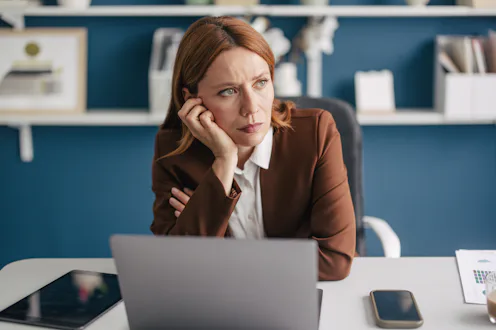 A thoughtful businesswoman with a pensive expression, resting her chin on her hand while contemplati...