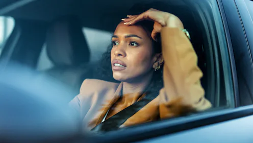 Female driver displaying anger and frustration while surrounded by vehicles. Traffic congestion, imp...