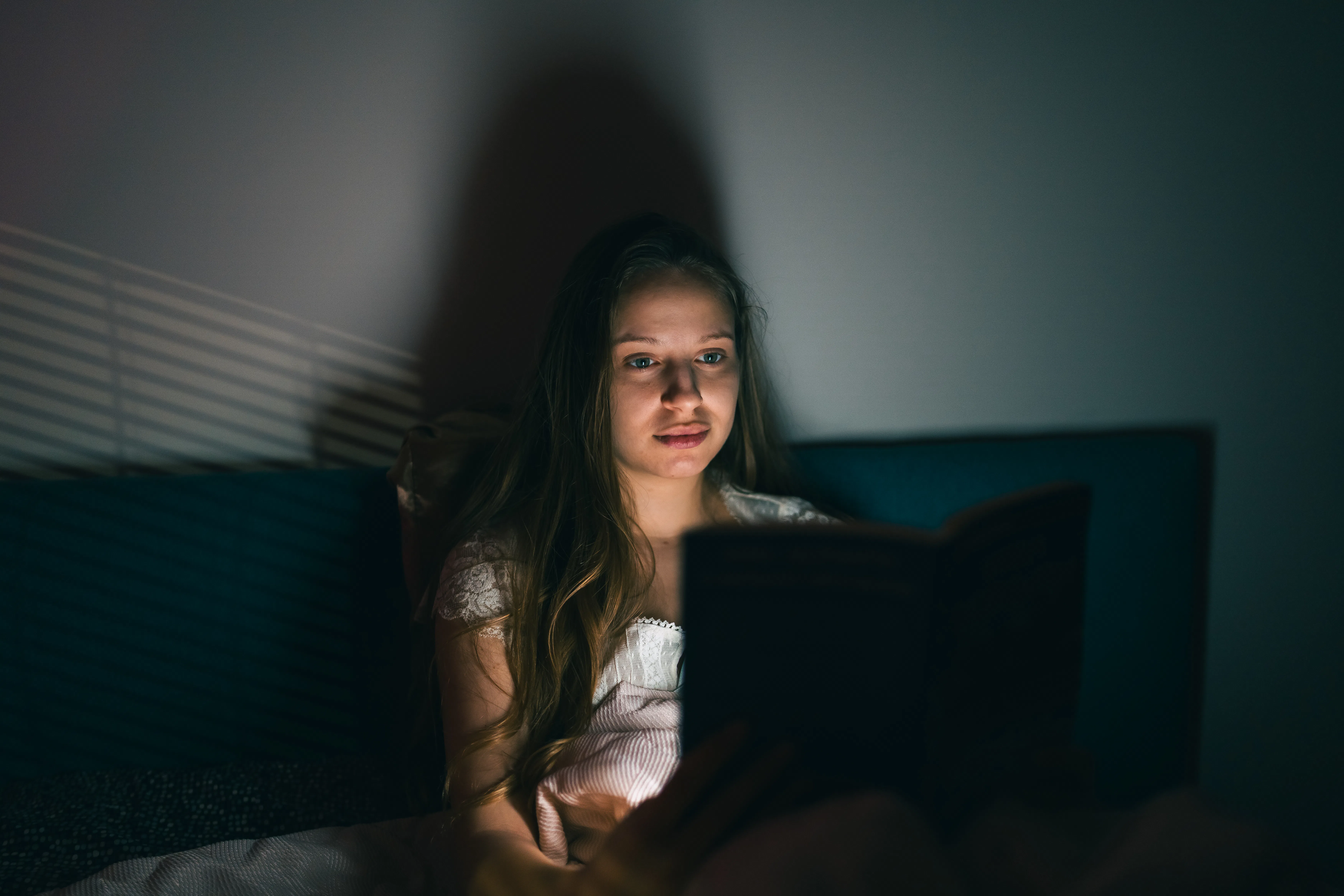 A woman lies in bed at night reading a book, immersed in her story, feeling relaxed and comfortable ...
