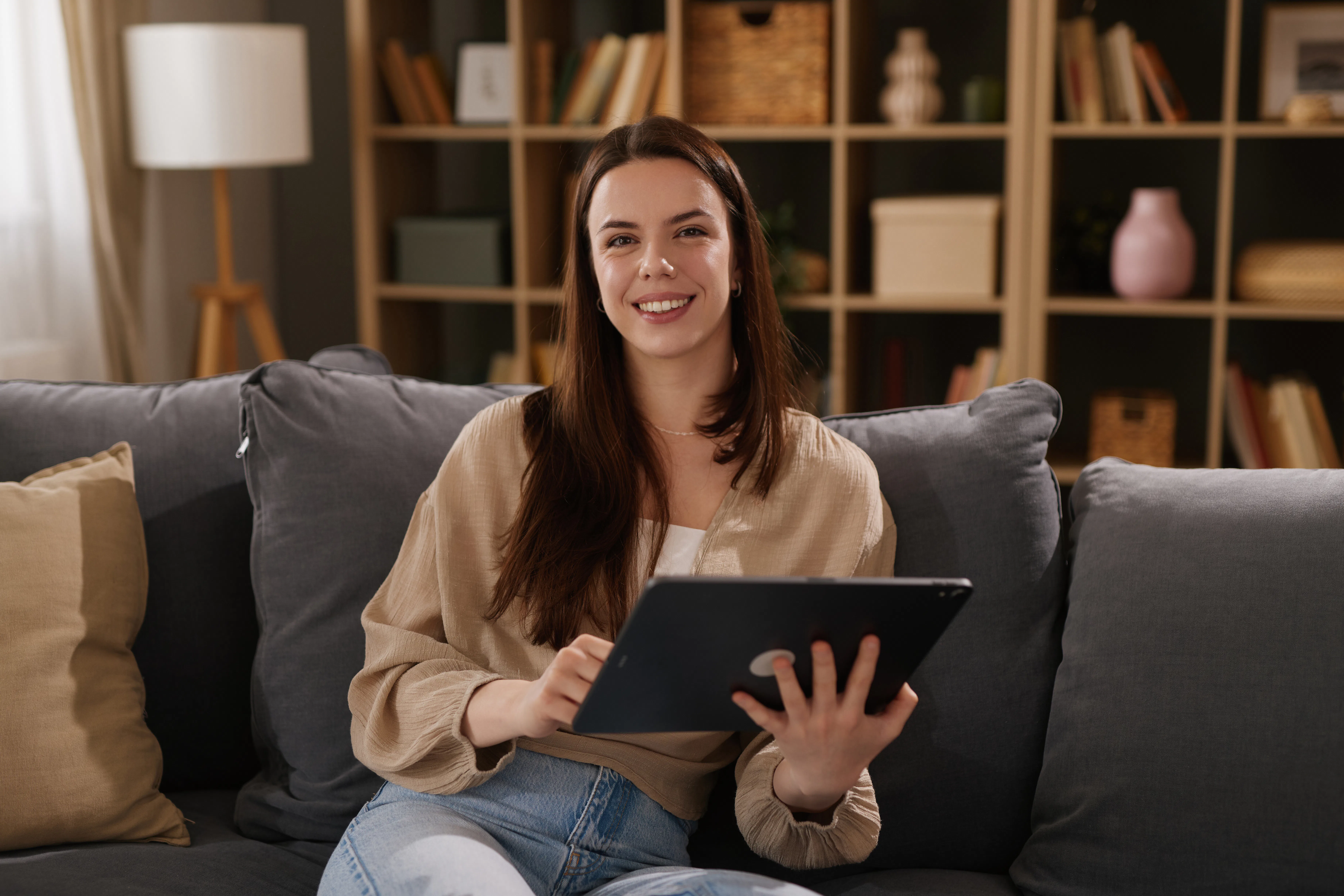 Young woman smiling, relaxing on couch while using a digital tablet at home