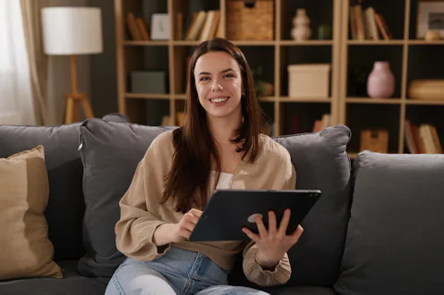 Young woman smiling, relaxing on couch while using a digital tablet at home
