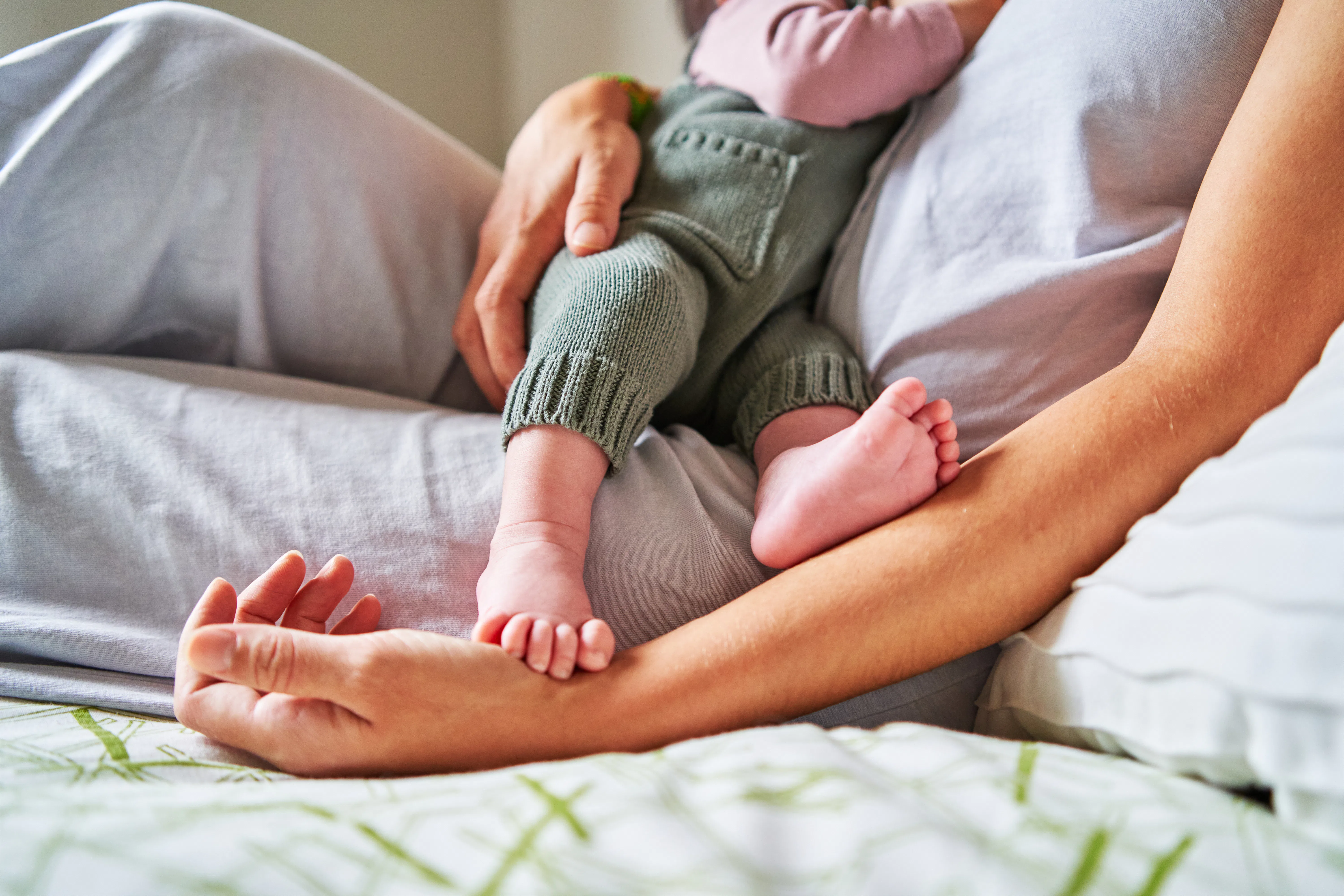 Cropped photo of an unrecognizable baby eating from mother's breast while lying in bed