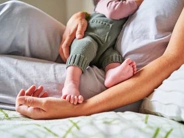 Cropped photo of an unrecognizable baby eating from mother's breast while lying in bed