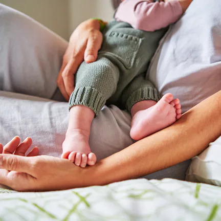 Cropped photo of an unrecognizable baby eating from mother's breast while lying in bed