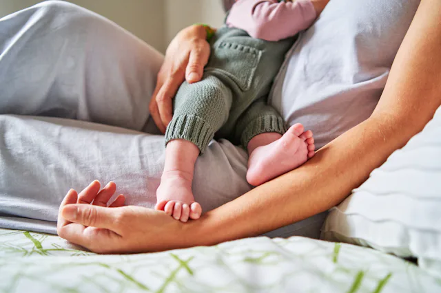 Cropped photo of an unrecognizable baby eating from mother's breast while lying in bed