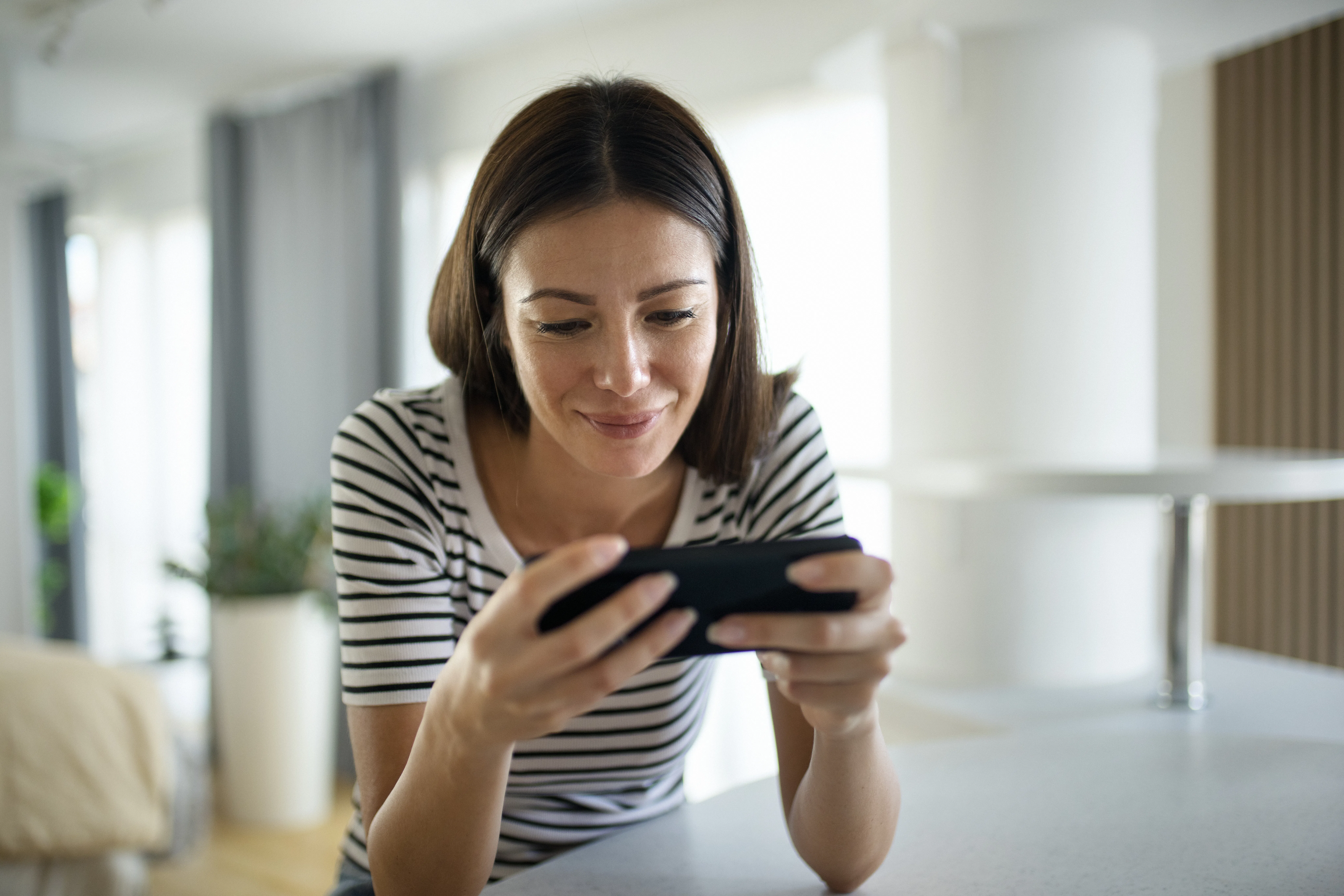 Closeup front view of a young woman playing video games on a smart phone at home.