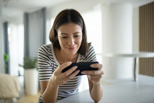 Closeup front view of a young woman playing video games on a smart phone at home.