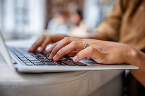 A student focuses on typing on a laptop in a contemporary study space. Soft lighting creates a warm ...