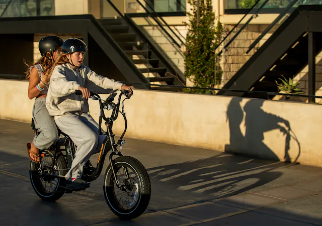 People ride an e-bike on the Strand in Hermosa Beach.