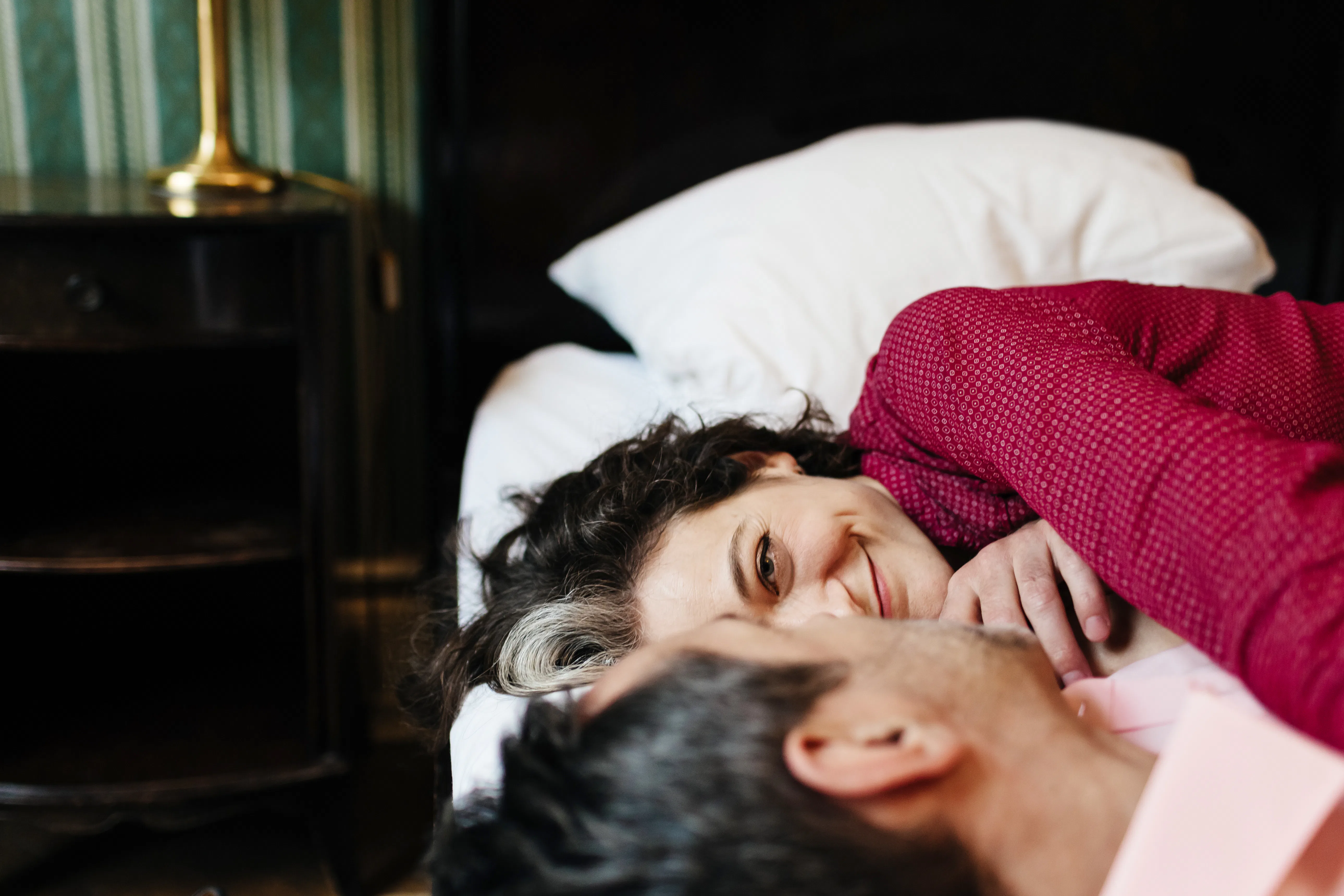 A mature, loving couple is looking at each other lying on a hotel bed. They seem to be in love as th...