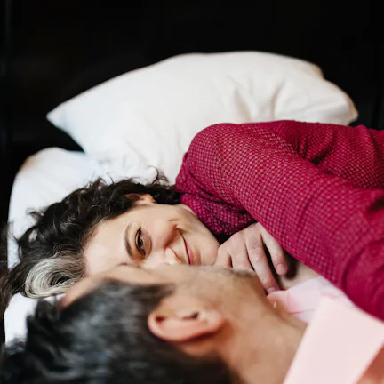 A mature, loving couple is looking at each other lying on a hotel bed. They seem to be in love as th...