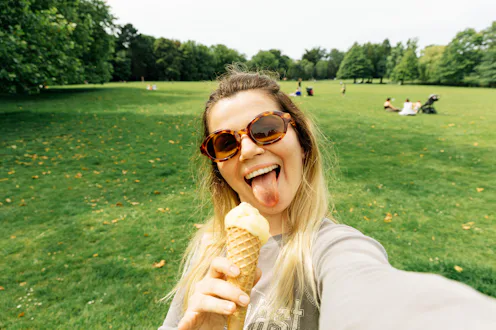 Young woman taking selfie with ice cream cone outdoors with green park in background. Summer refresh...