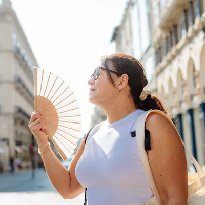 Mature woman suffering heat stroke in the city streets, using han fan, climate change, heat wave or summer high temperatures