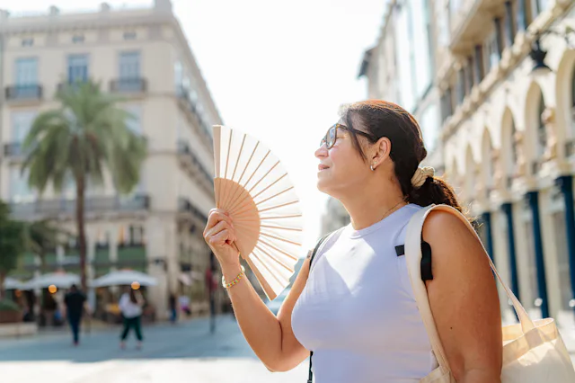 Mature woman suffering heat stroke in the city streets, using han fan, climate change, heat wave or ...
