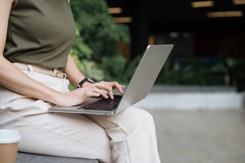Mature businesswoman using a laptop in an office green space outdoors, combining productivity with t...