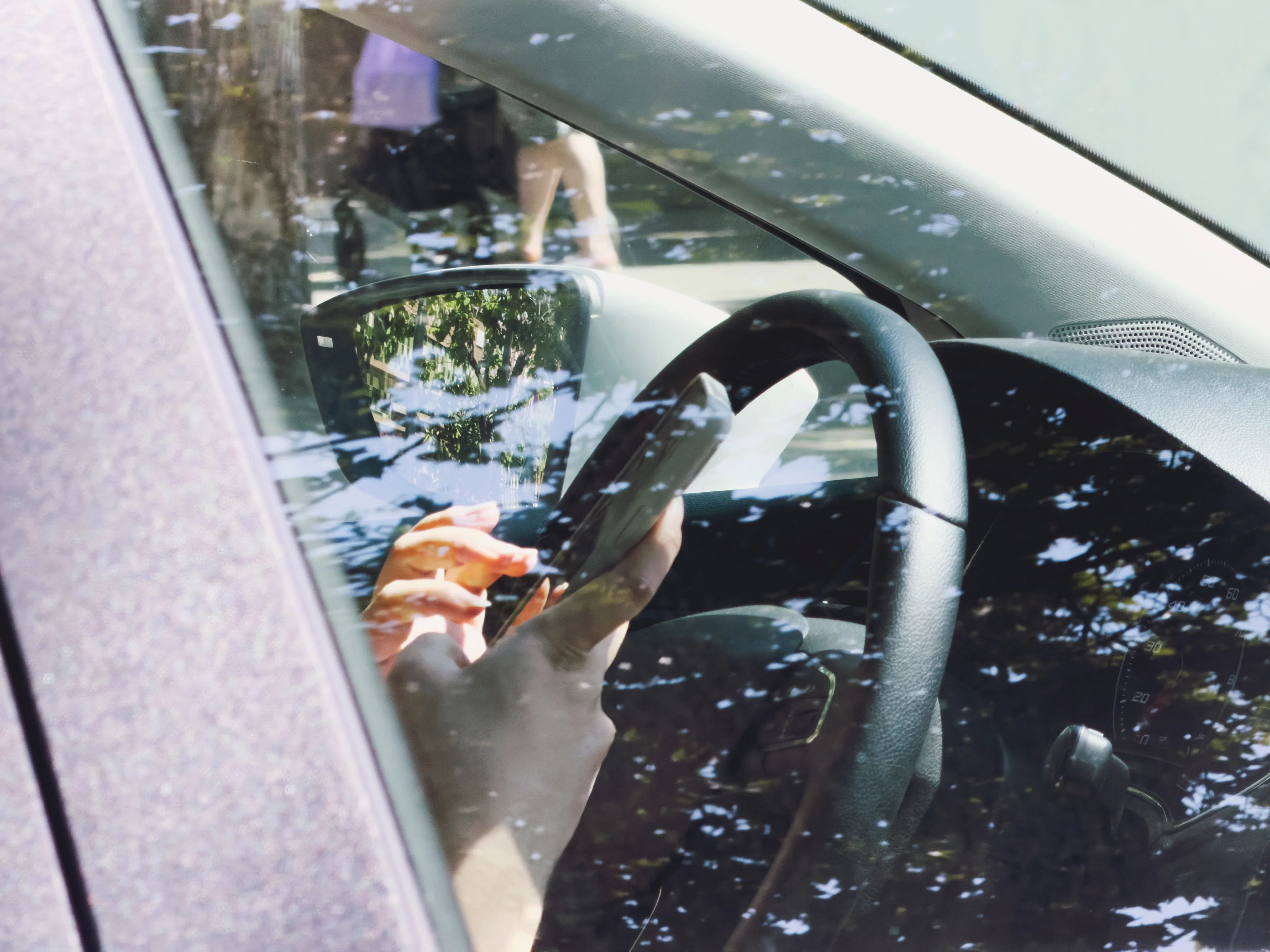Close-up of a driver holding and using a smartphone behind the steering wheel inside a car, highligh...