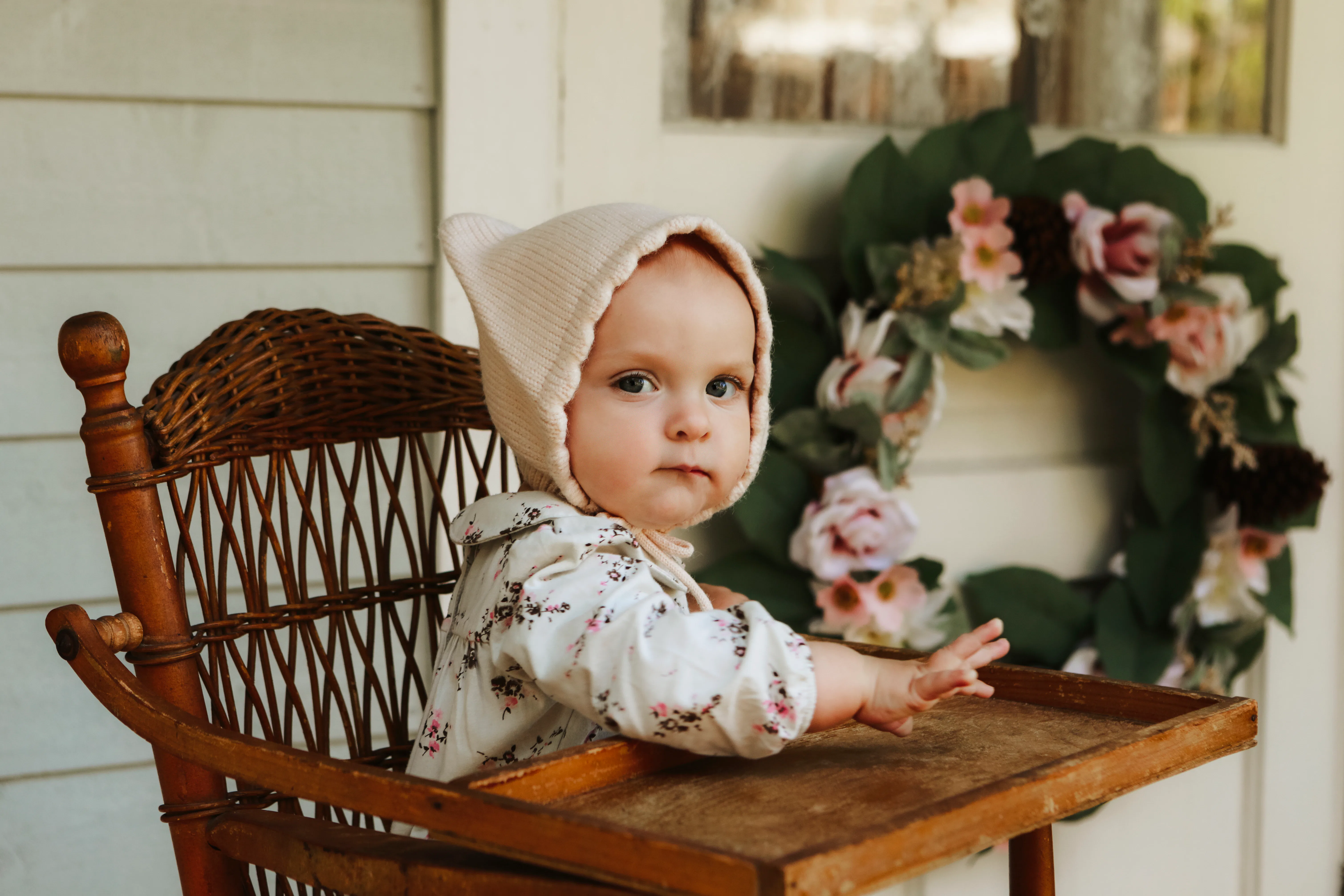 An adorable baby girl, nine months old, sitting in a high chair on the porch of a charming cottage. ...