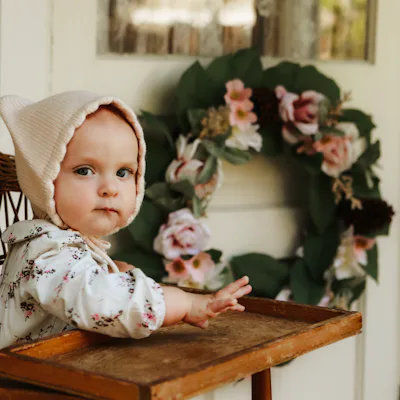 An adorable baby girl, nine months old, sitting in a high chair on the porch of a charming cottage. Shot with a Canon 5D Mark IV.