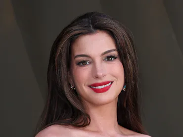 Anne Hathaway attends the world premiere of "The Odyssey" in London, wearing a red lip and smiling a...