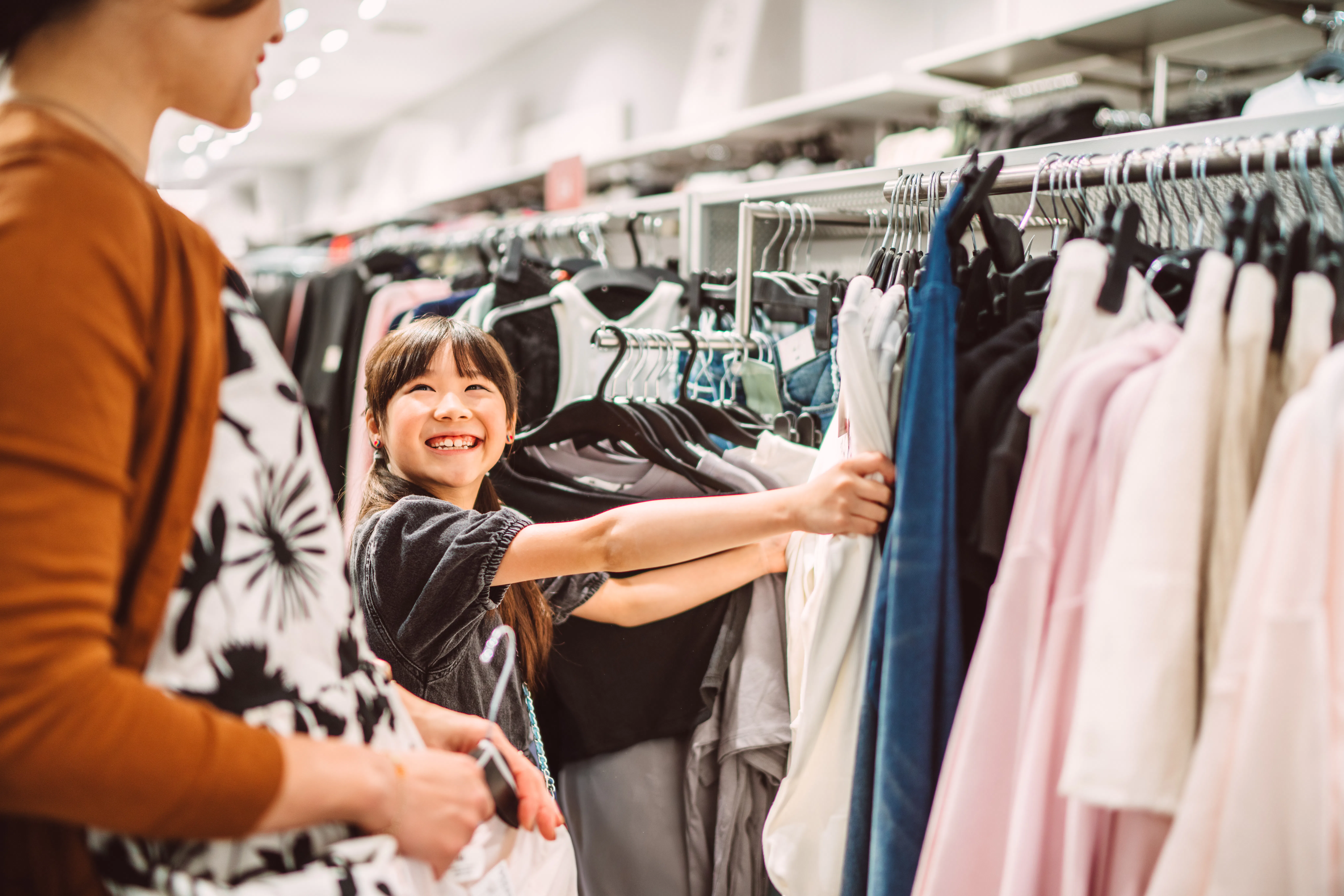 Happy mother and daughter shopping together for clothes in a fashion retail store. The young girl is...
