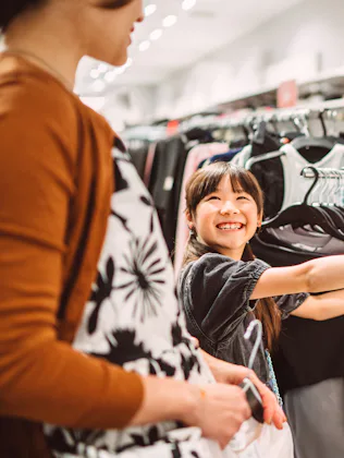 Happy mother and daughter shopping together for clothes in a fashion retail store. The young girl is...