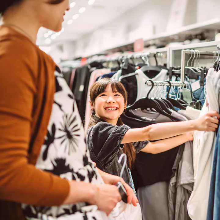 Happy mother and daughter shopping together for clothes in a fashion retail store. The young girl is...