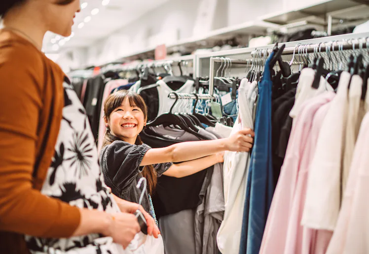 Happy mother and daughter shopping together for clothes in a fashion retail store. The young girl is...