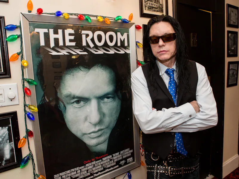 NEW ORLEANS, LA - DECEMBER 05: Tommy Wiseau poses next to a poster for 'The Room' at 'The Room' scr...