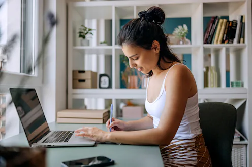 Young beautiful businesswoman taking notes while working at home office