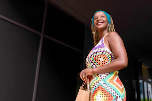 Happy black woman holding brown shopping bags, smiling joyfully after a successful retail therapy ex...