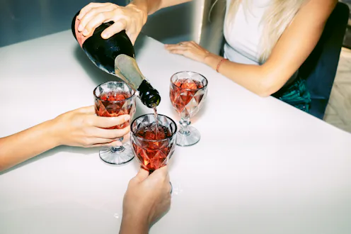 Unrecognizable female friends celebrate and drink red sparkling wine