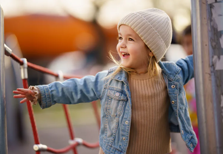 Smiling little girl enjoying playing on climbing frame at playground.