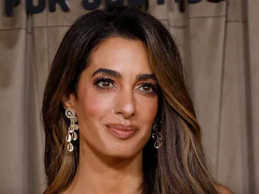 Amal Clooney at an event in London with long brown hair, brown makeup, and a brown dress