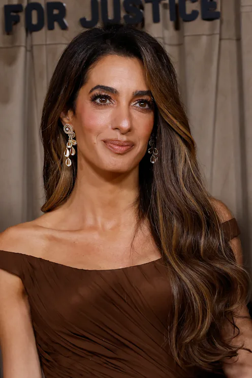 Amal Clooney at an event in London with long brown hair, brown makeup, and a brown dress