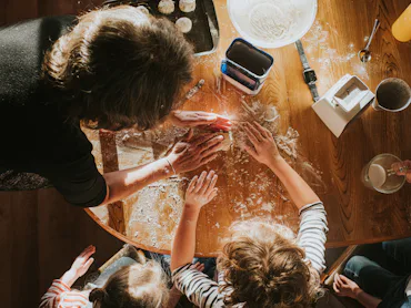Top down image of three children baking scones with thier grandmother. The scene is messy and busy.