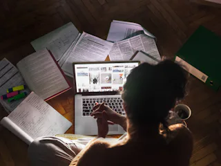 A woman with OCD sitting in a dark room while using her laptop and being surrounded by various books
