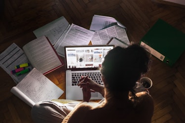 A woman with OCD sitting in a dark room while using her laptop and being surrounded by various books