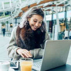 A young woman with long hair smiling while using a laptop in the cafe