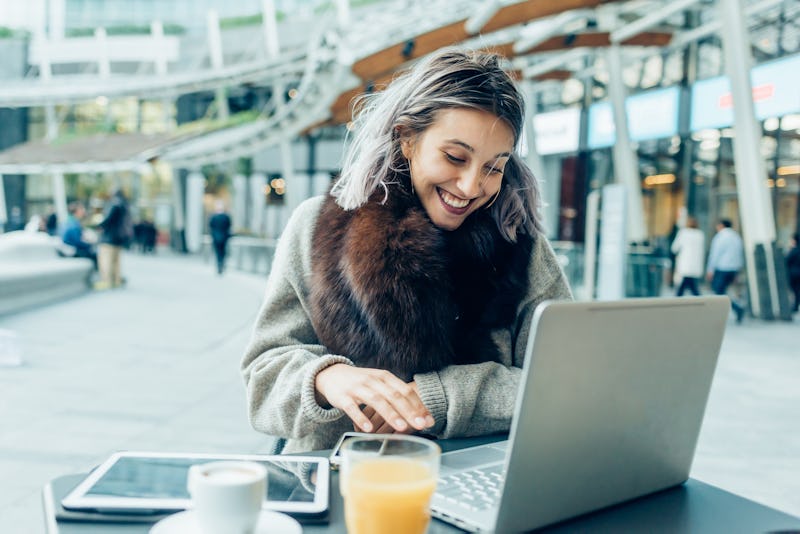 A young woman with long hair smiling while using a laptop in the cafe