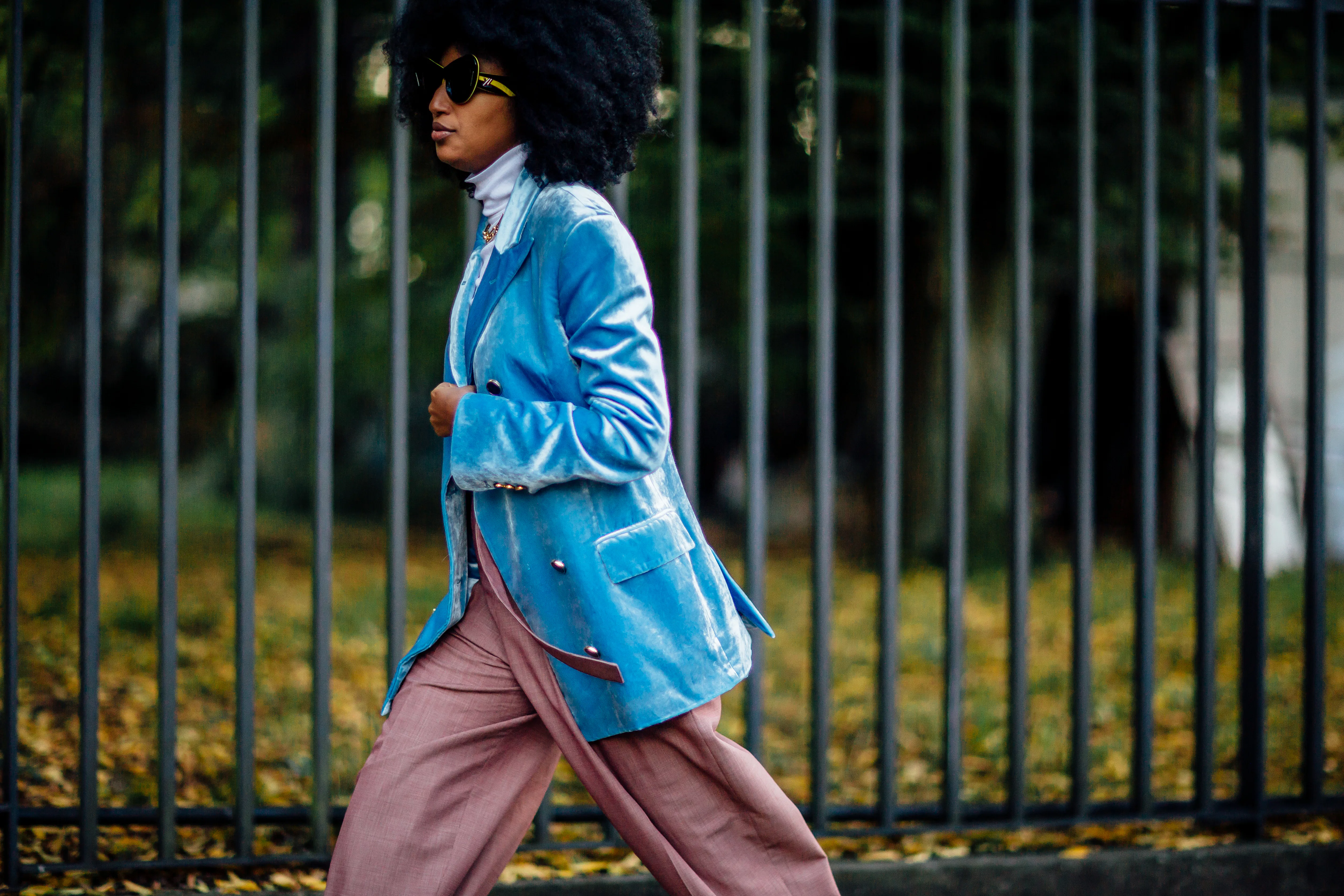 A woman with afro hair wearing a blue oversized blazer over a white turtleneck and pink satin pants ...