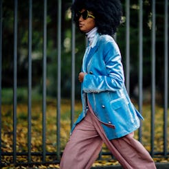 A woman with afro hair wearing a blue oversized blazer over a white turtleneck and pink satin pants ...