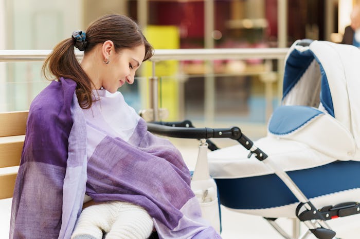 A woman standing next to a stroller in public and breastfeeding