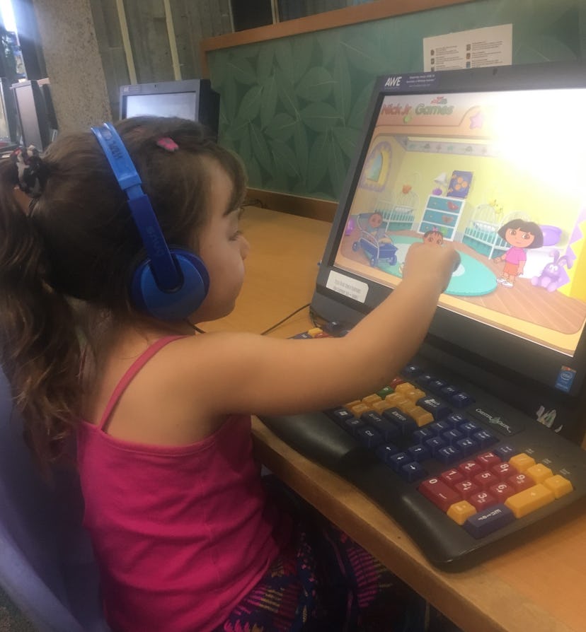 A little girl with headphones playing a game on her computer