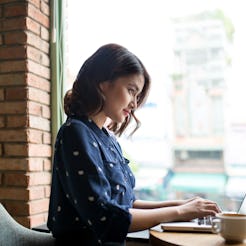 A young woman working on her laptop in a coffee shop during a cloudy day