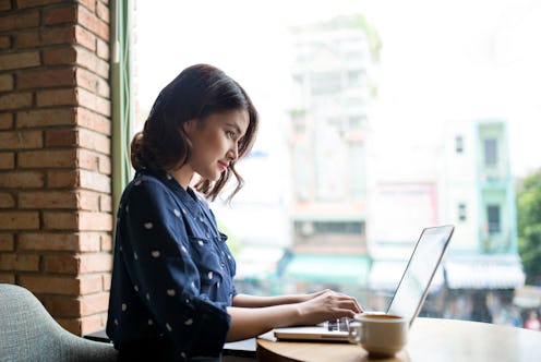 A young woman working on her laptop in a coffee shop during a cloudy day