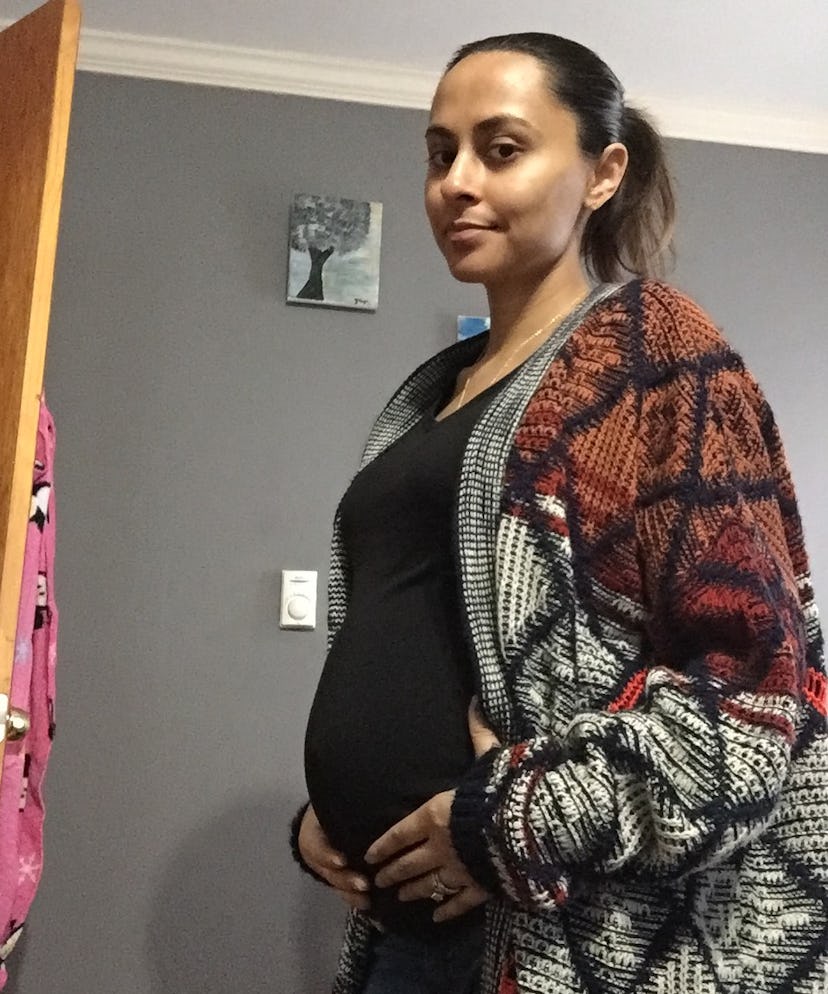 Pregnant Yasmine Singh wearing a black t-shirt and a cozy sweater while holding her belly