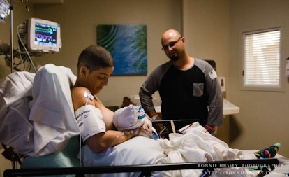 Short hair woman breastfeeding her child while battling breast cancer, and her proud husband watchin...