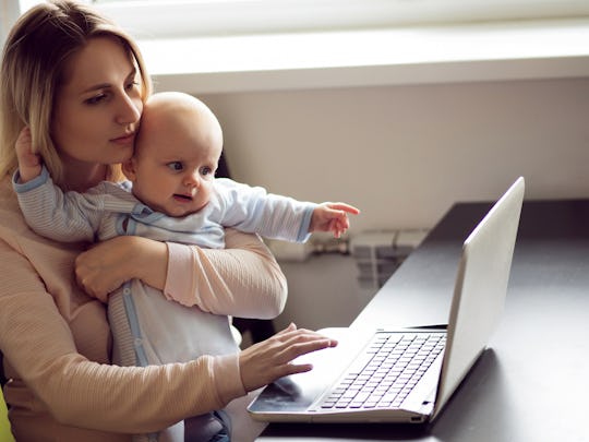 Mom on maternity leave holding her baby and using the laptop